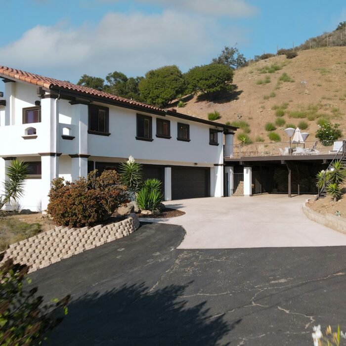 Modern concrete driveway installation leading to a white two-car garage of a brown ranch-style home under a clear blue sky.