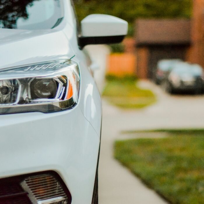 Close-up of a clean white car parked on a smooth concrete residential driveway with a blurred suburban house in the background.
